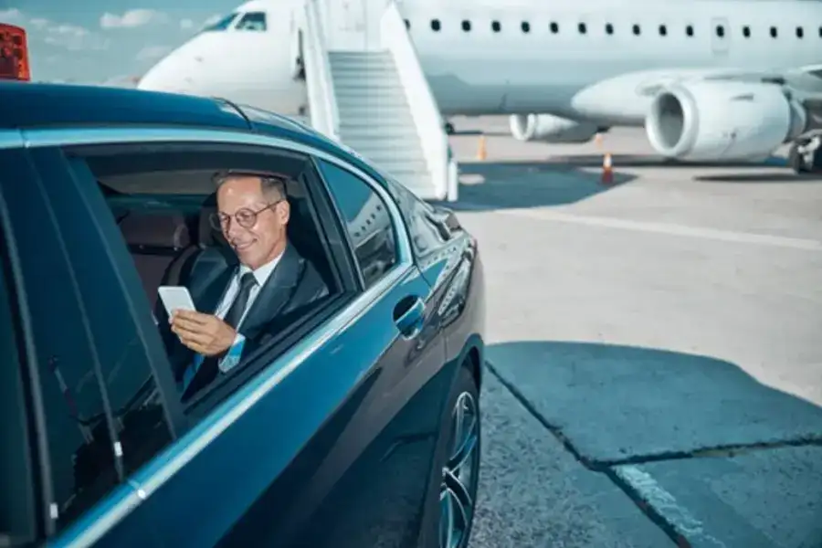 A businessman is seen getting into a black car as it leaves the airport tarmac, with a parked airplane visible in the background. Symbolizing San Antonio Black Car Service.